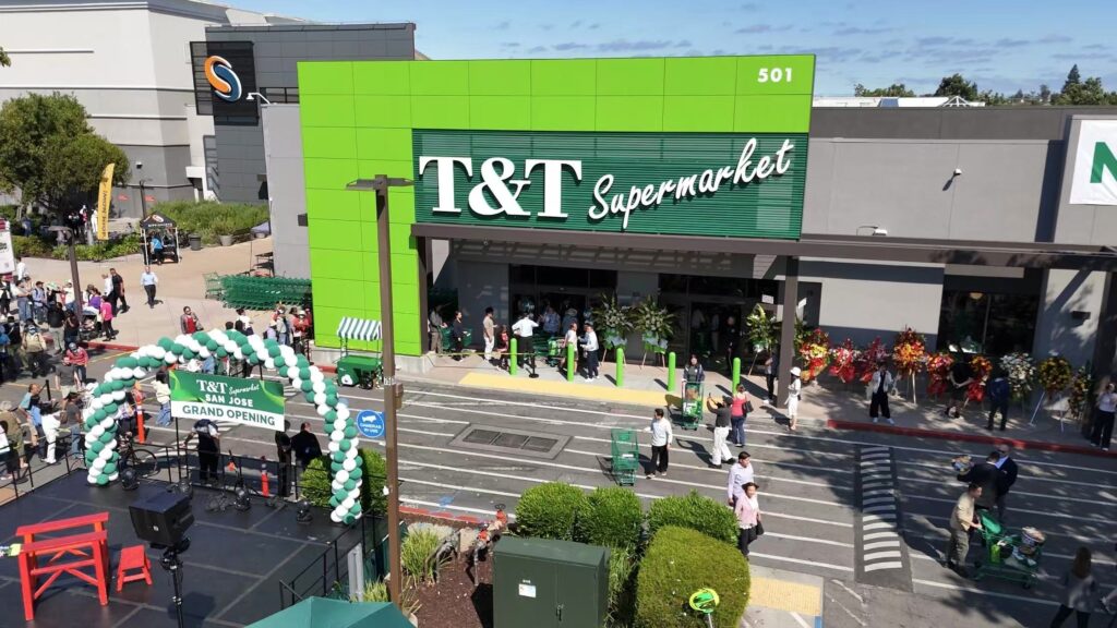 T&T Supermarket's exterior at Westgate Center in San José on grand-opening day, June 2026, with a crowd and a green-and-white balloon arch.